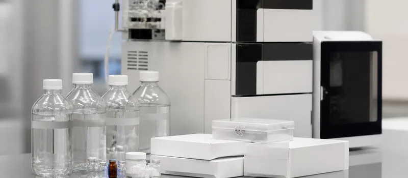 Sealed analytical chemicals and standards beside HPLC equipment.